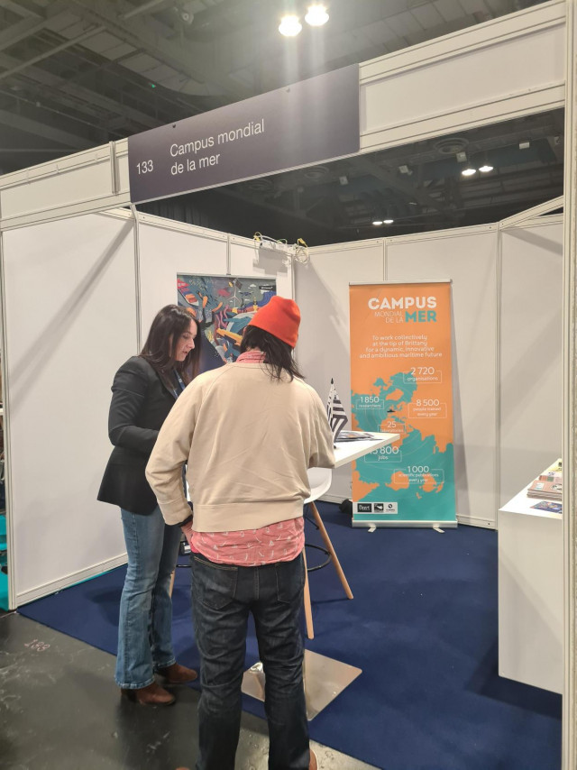 Photo taken at the Campus Mondial de la Mer stand during the Ocean Sciences Meeting. Emmanuelle and Daphnée welcome visitors and present Sea Tech Week, engaging with participants about the activities and initiatives led by the Campus.