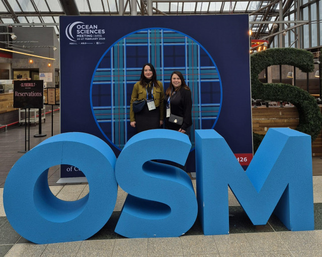 Emmanuelle and Daphnée pose in front of the Ocean Sciences Meeting logo, representing the Campus Mondial de la Mer and welcoming participants to present Sea Tech Week.